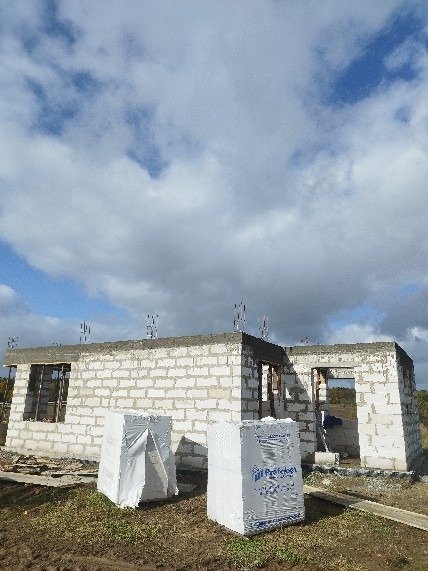 Budowa domu z białych bloczków, widoczne zbrojenia i dwa opakowania materiałów budowlanych na pierwszym planie. Pochmurne niebo w tle.