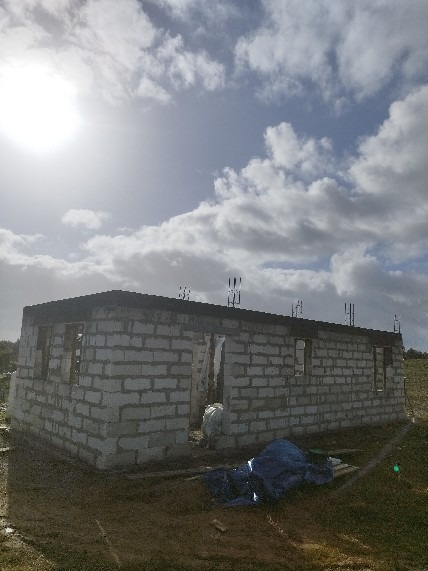 Surowy stan budynku z białych bloczków, widoczne zbrojenia na dachu, błękitne niebo z chmurami w tle. Budowa w toku, materiały budowlane przy budynku.