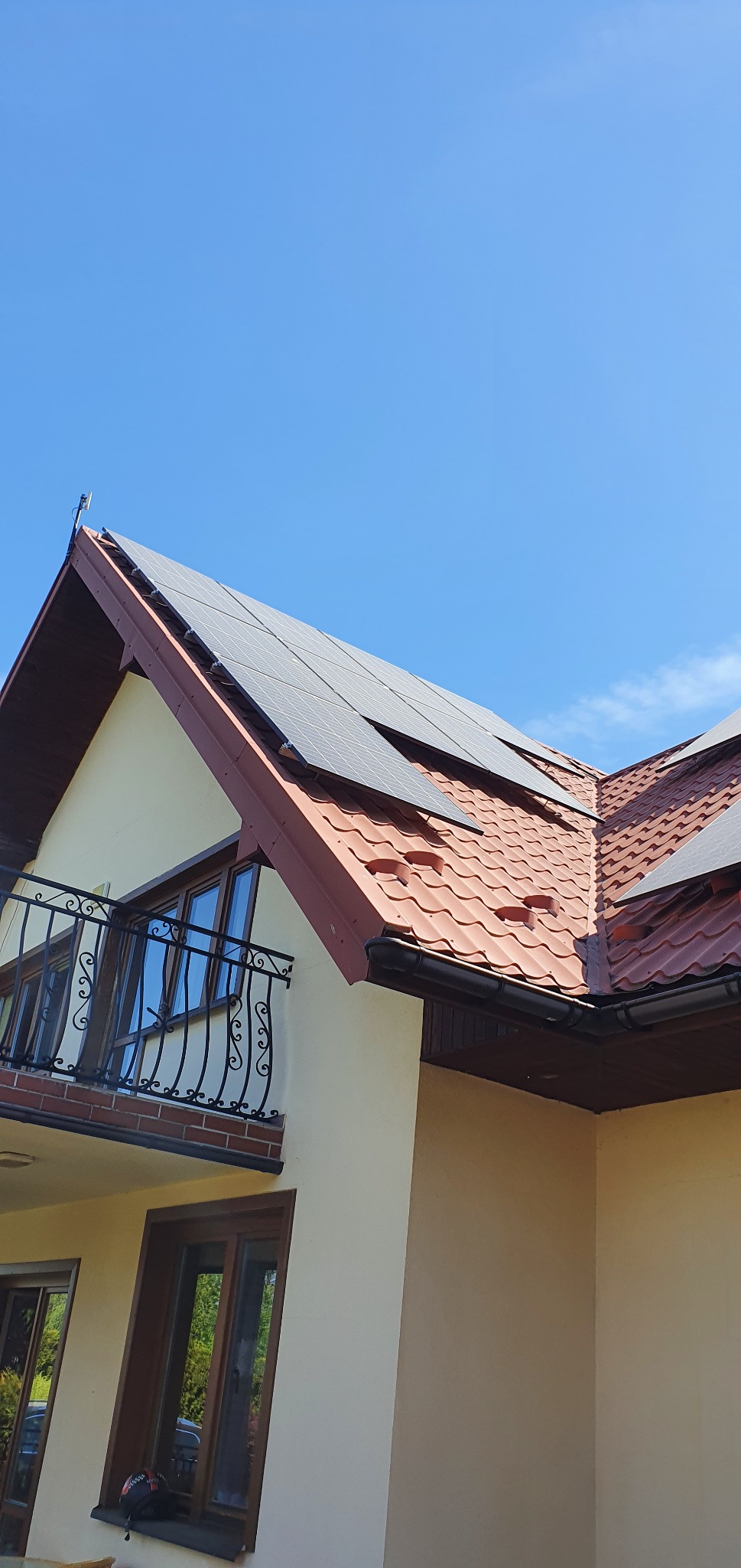 Panele słoneczne zamontowane na dachu domu jednorodzinnego z czerwoną dachówką, widok z dołu na błękitne niebo.