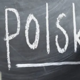 Napis 'Polski' pisany kredą na tablicy, obok leżą książki i długopis.