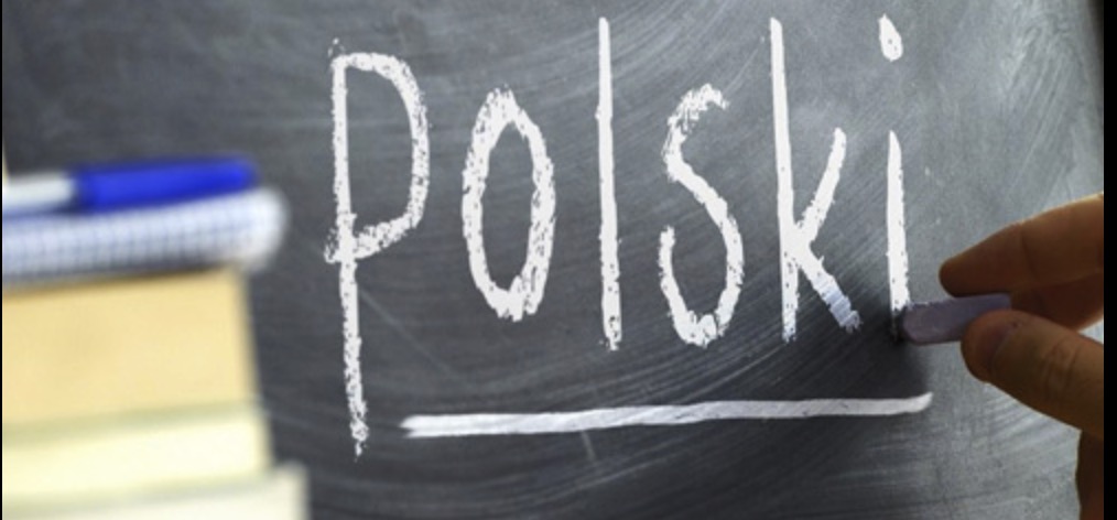 Napis 'Polski' pisany kredą na tablicy, obok leżą książki i długopis.