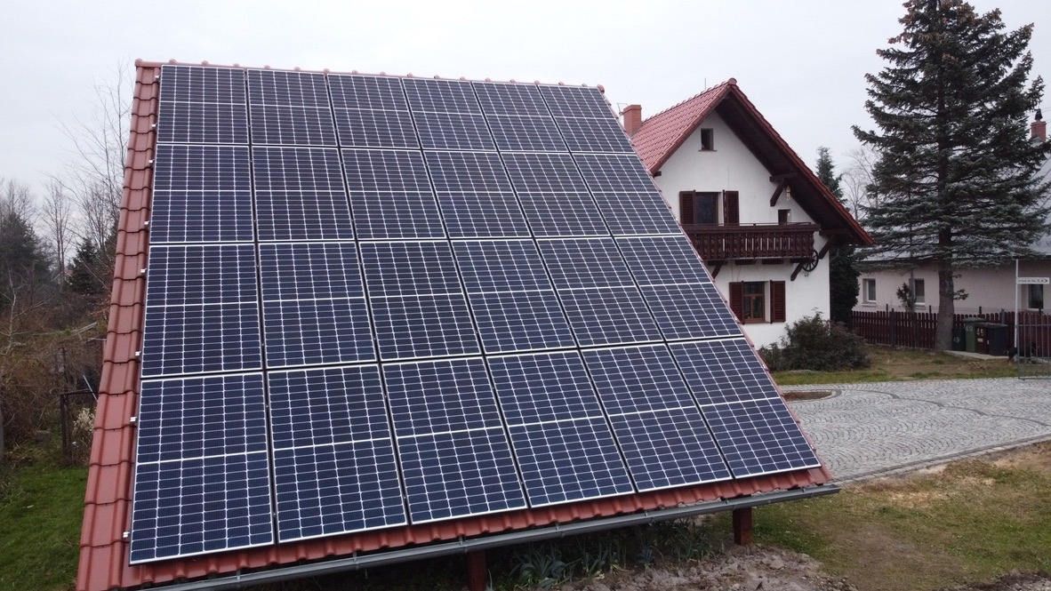 Panele słoneczne na dachu domu z czerwoną dachówką, widok z dołu, pochmurny dzień.