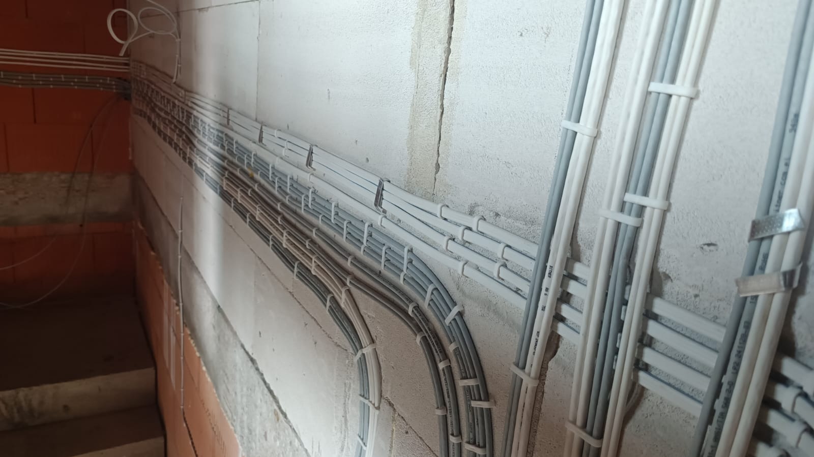 Instalacja przewodów elektrycznych i rur w ścianie budynku w trakcie budowy. Przewody i rury przymocowane do ściany za pomocą uchwytów.