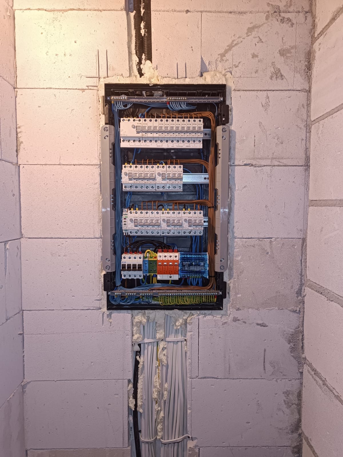 Rozdzielnica elektryczna zamontowana w ścianie z betonu komórkowego, widoczne kable i zabezpieczenia. Instalacja w trakcie prac wykończeniowych.