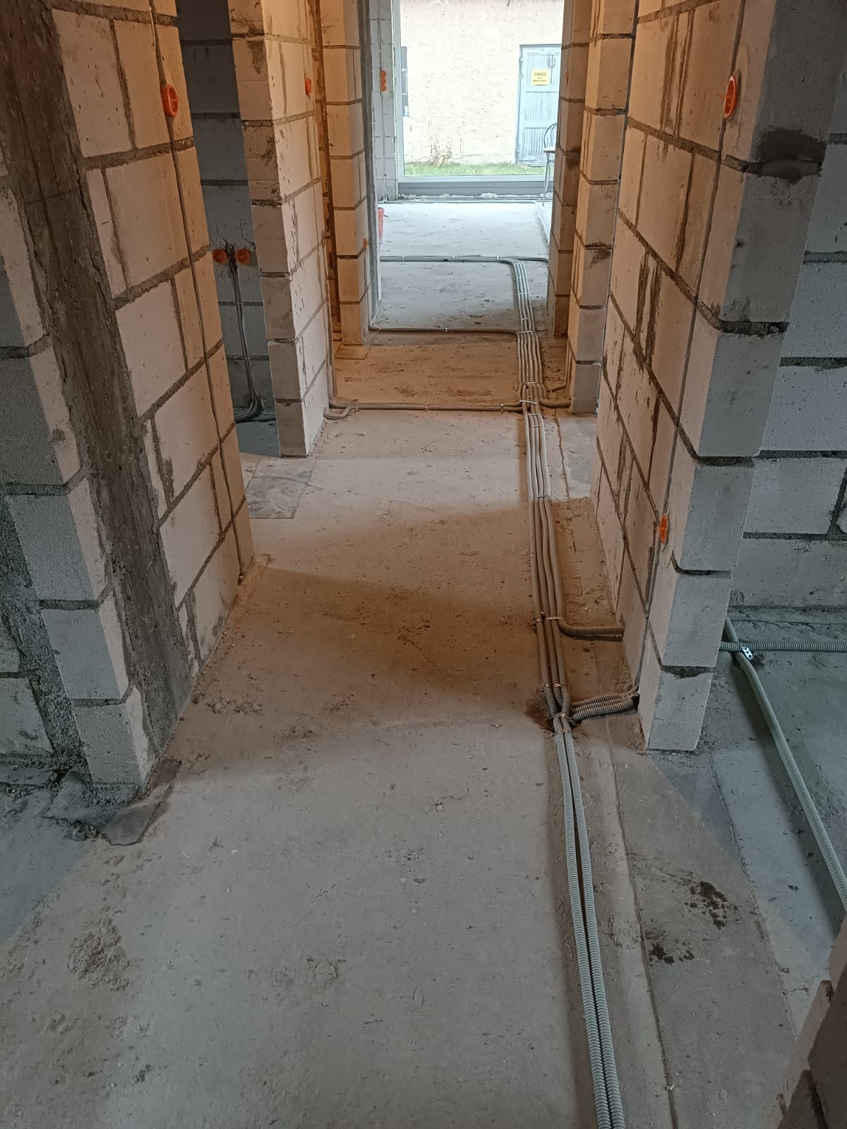 Surowy stan domu z szarego bloczka: widoczne korytarze i instalacje elektryczne w peszlach na podłodze, czerwone puszki w ścianach. W tle widoczne otwarte przestrzenie.