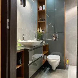 Nowoczesna łazienka z szarą armaturą i marmurowymi płytkami, wisząca umywalka na szafce z lustrzanym frontem, podwieszana toaleta i oświetlenie punktowe.