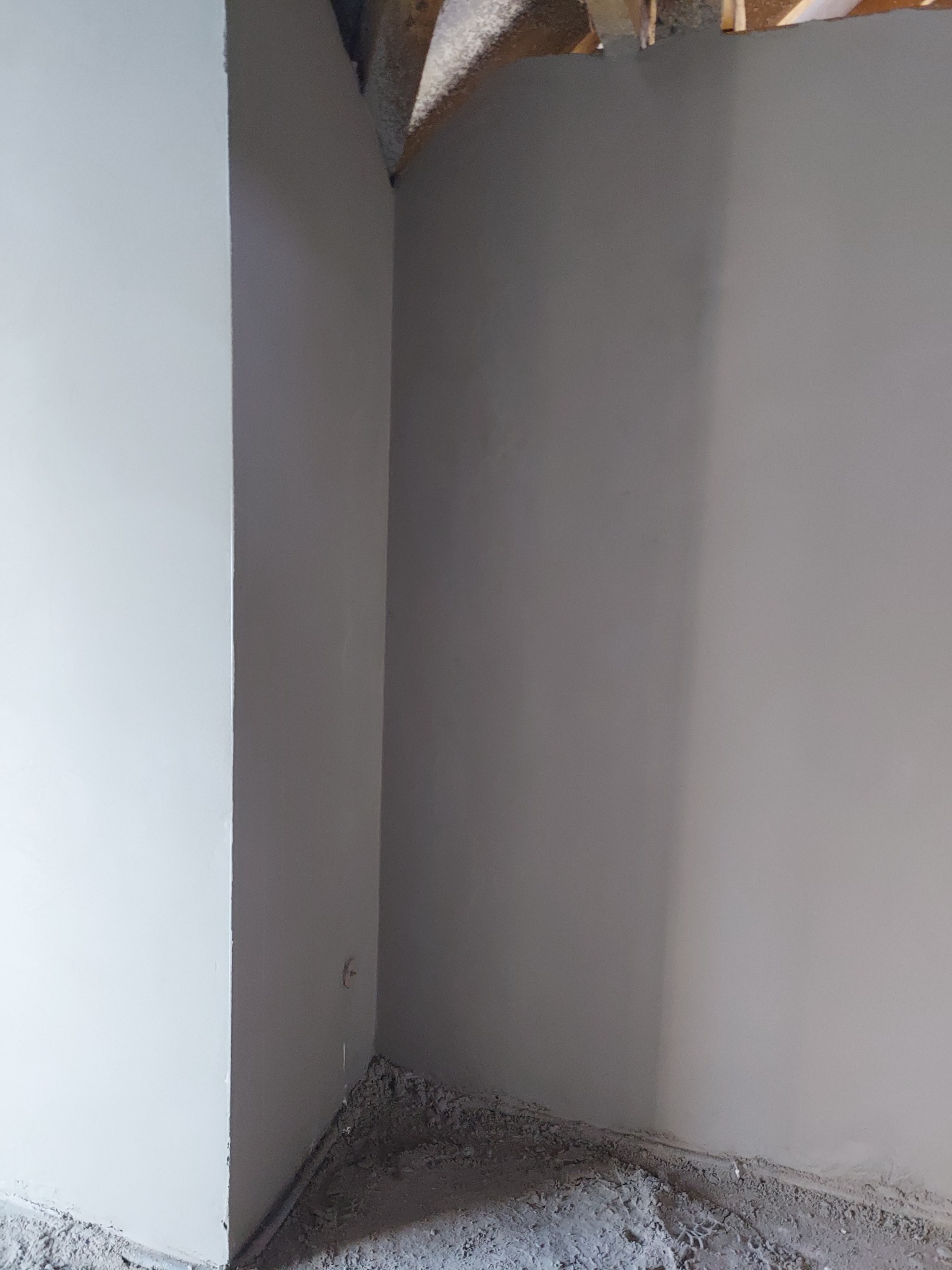 Świeżo otynkowany narożnik pomieszczenia z widocznymi śladami zaprawy na podłodze i surowym wykończeniem stropu.