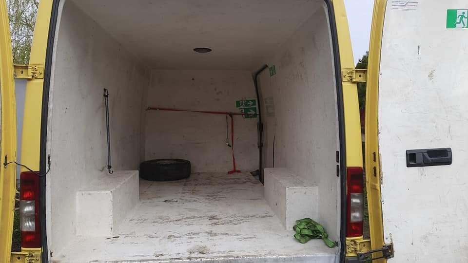 Wnętrze puste, żółtego busa z otwartymi drzwiami; widoczne opony, pasy transportowe, oraz tabliczka z symbolem ewakuacyjnym.