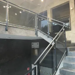 Szklane balustrady z metalową ramą w nowoczesnym wnętrzu klatki schodowej w Żarkach, widoczne szafki pracownicze i oświetlenie sufitowe.