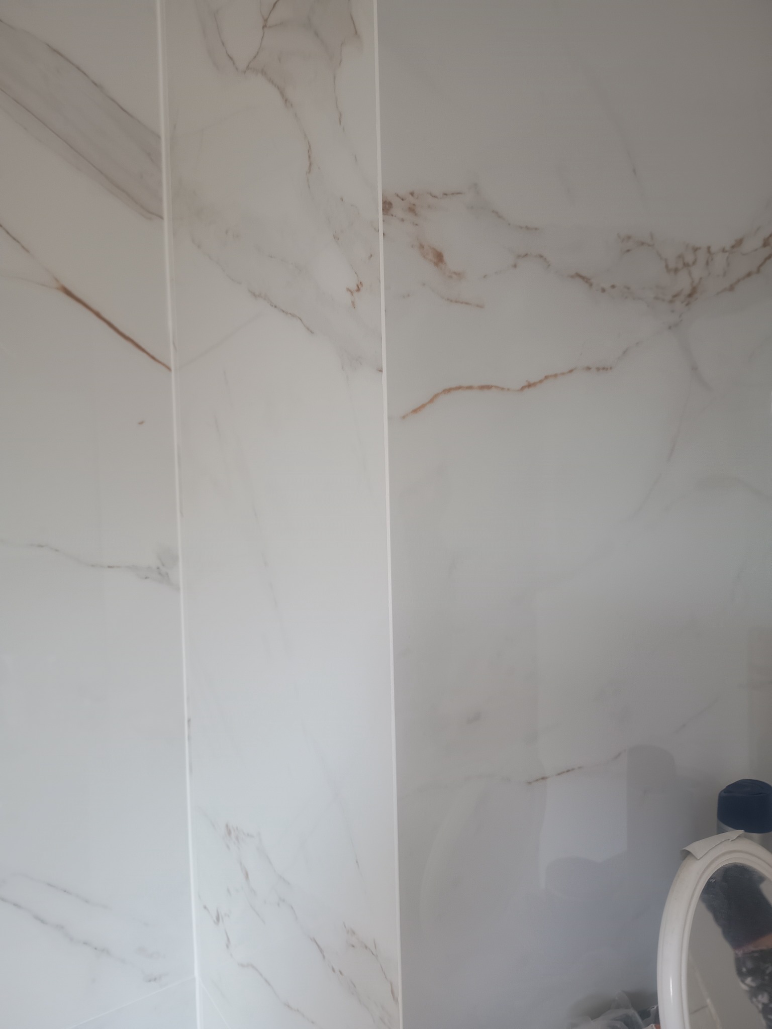 Białe płytki imitujące marmur z delikatnym złotym żyłowaniem, ułożone w łazience w Stawigudzie, widoczne fragmenty akcesoriów łazienkowych.