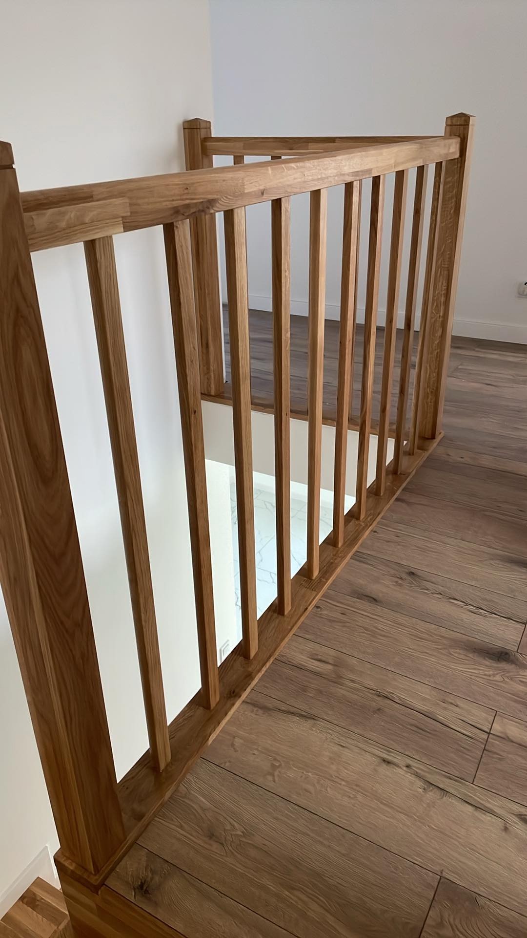Drewniana balustrada schodowa z prostymi szczeblami, widok z góry na parkiet, białe ściany w tle.
