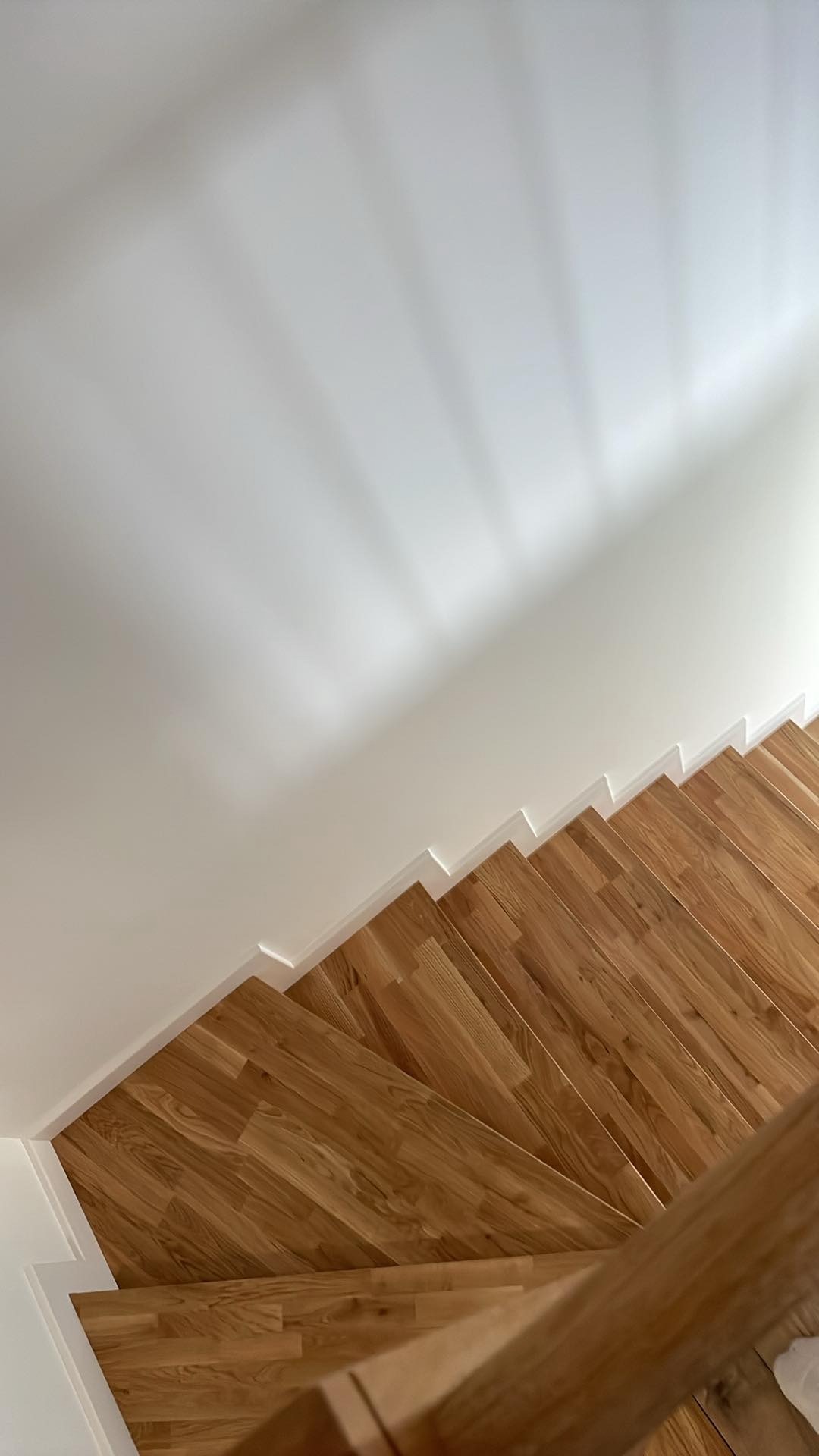 Drewniane schody z parkietu dębowego, widok z góry, jasne ściany z listwami przypodłogowymi, cień na ścianie.