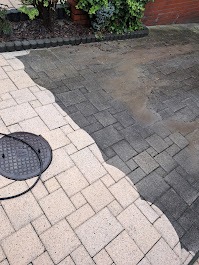 Częściowo wyczyszczona kostka brukowa z widocznym włazem kanalizacyjnym, ukazująca różnicę przed i po myciu, z zielenią w tle.