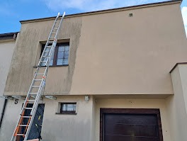 Fragment elewacji domu w trakcie czyszczenia, widoczna drabina oparta o ścianę, kontrast między umytą a brudną powierzchnią.
