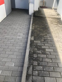 Częściowo wyczyszczona szara kostka brukowa, widoczna różnica między umytą a zabrudzoną powierzchnią, na granicy widoczny brudny odpływ liniowy.