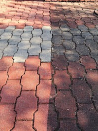 Częściowo oczyszczona, czerwono-szara kostka brukowa, widoczna różnica w kolorze i czystości między wyczyszczoną a zabrudzoną powierzchnią.