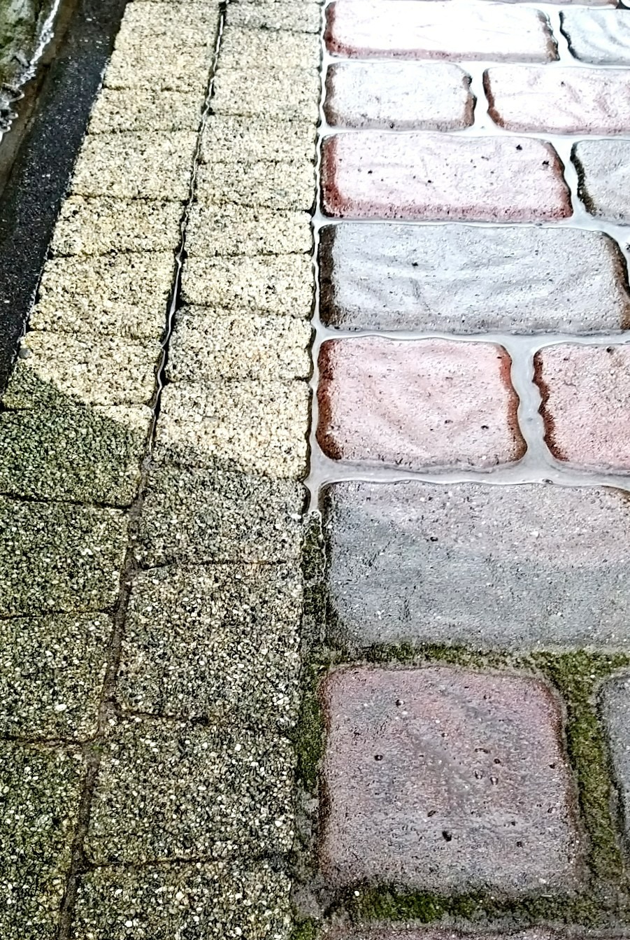 Częściowo wyczyszczona kostka brukowa, z wyraźną różnicą w kolorze i czystości między czystą a zabrudzoną powierzchnią, z widocznymi śladami wody.
