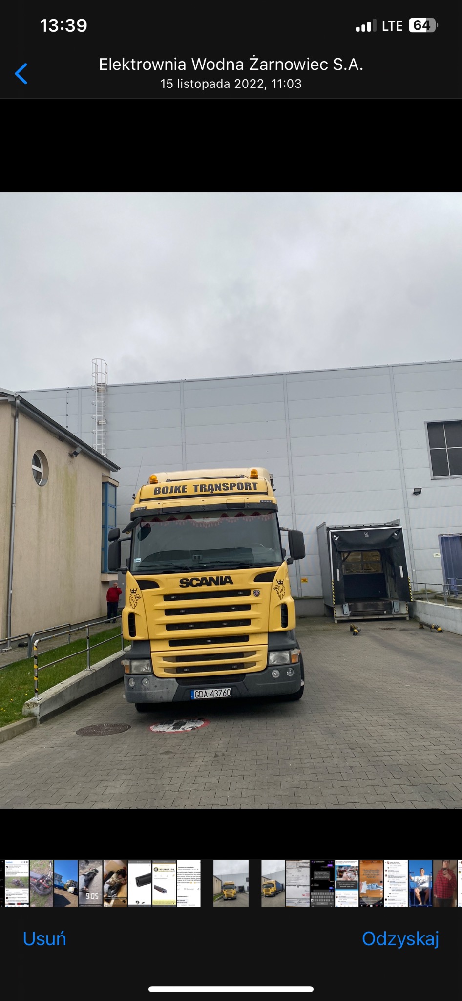 Żółta ciężarówka marki Scania firmy Bojke Transport zaparkowana przed magazynem z otwartą rampą załadunkową w pochmurny dzień.