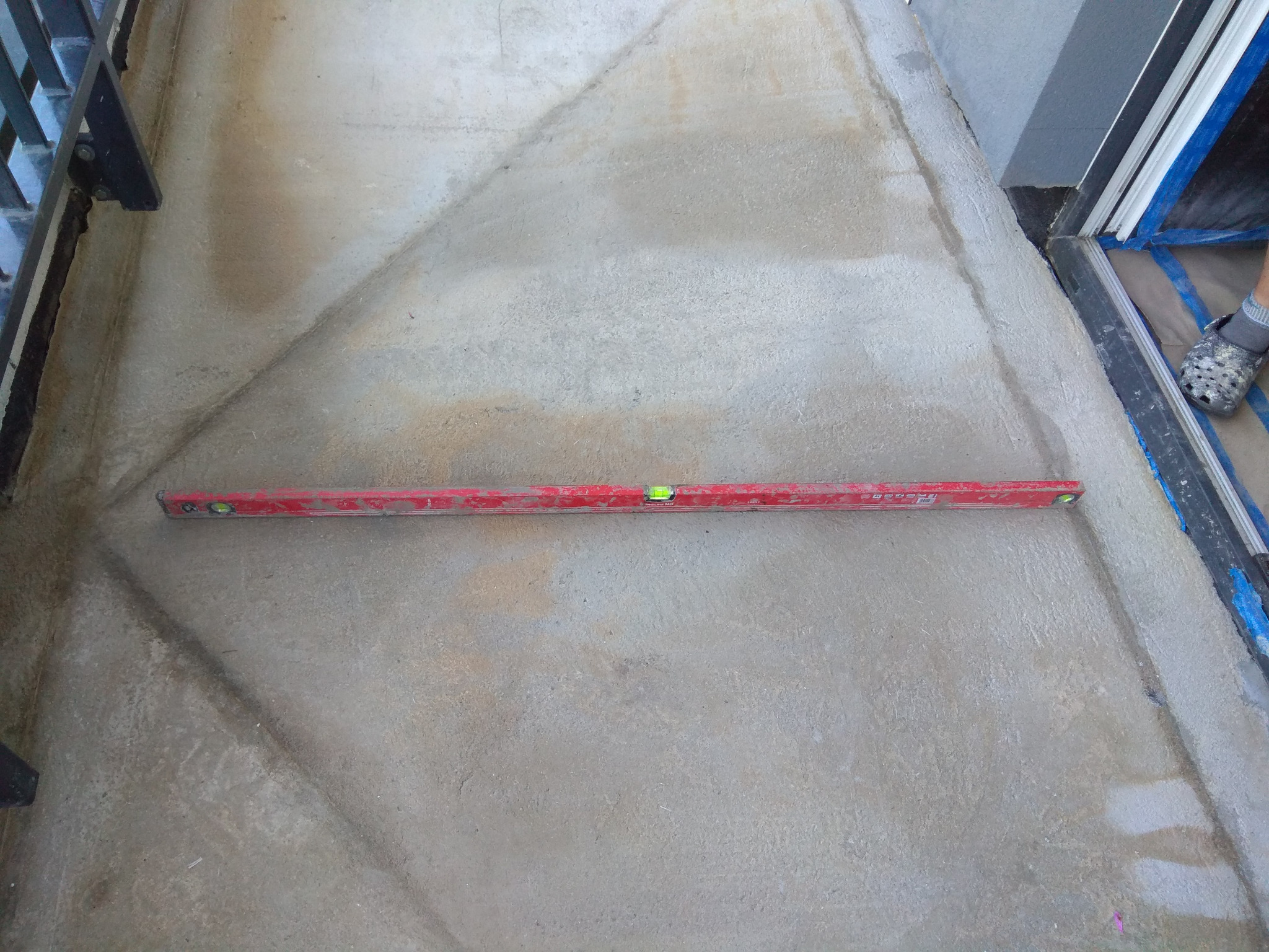 Poziomica spoczywa na świeżo wylanym betonie, wyrównywanie powierzchni wzdłuż ramy okiennej.