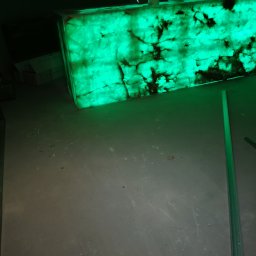 DP FENSTERTECHNIK - Podświetlony od spodu blat z onyksu w zielonej tonacji, widoczne ciemne żyły kamienia, surowy beton na podłodze, listwa przypodłogowa.