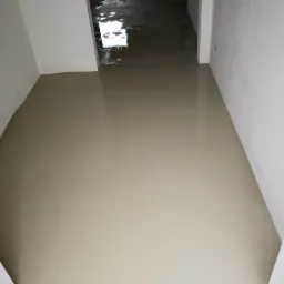 Świeżo wylana, gładka wylewka samopoziomująca na podłodze w trakcie remontu mieszkania, widoczna w perspektywie korytarza z białymi ścianami i odblaskami światła.