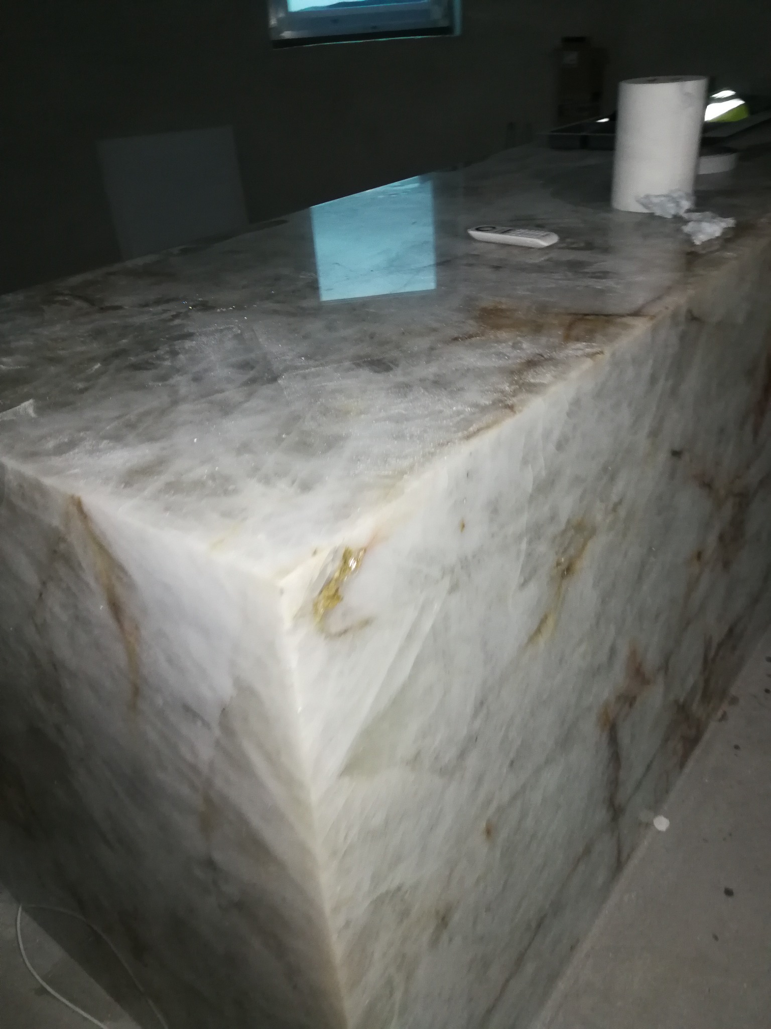 Wykończony blat z białego marmuru z brązowymi żyłkami, na nim pilot i rolka papieru, widoczne niedoskonałości wykończenia.