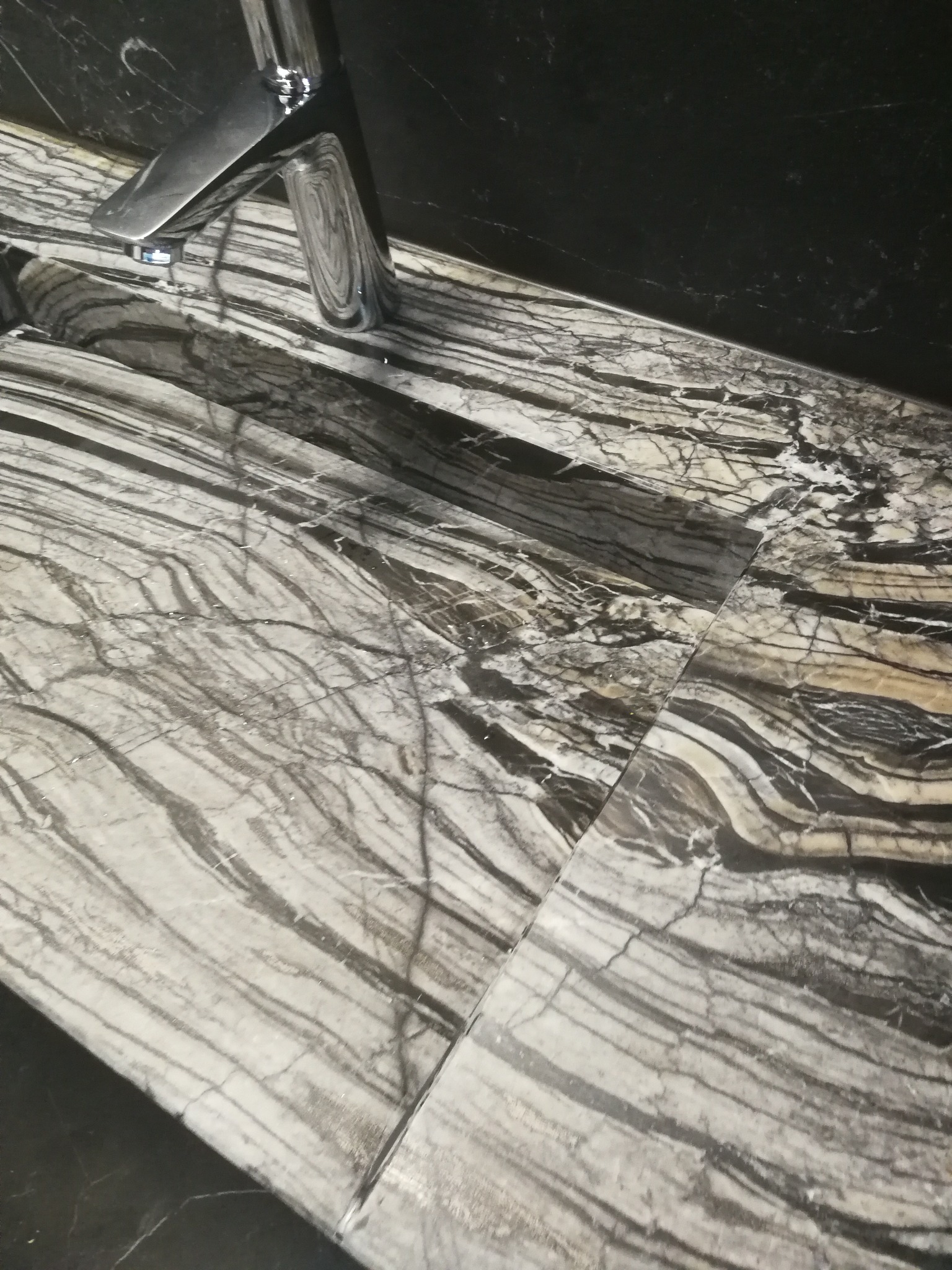 Bateria umywalkowa zamontowana na blacie z szarego marmuru z wyraźnym, żyłkowanym wzorem, widoczne połączenie płyt blatu.