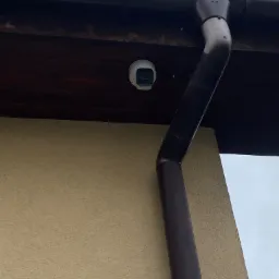 Kamera monitoringu zewnętrznego, kopułkowa, zamontowana pod okapem domu, widoczna rynna spustowa.