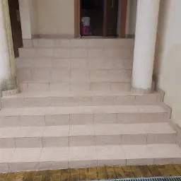 Kafelkowane schody wejściowe z kolumnami, widoczny kubeł w tle, lekko zabrudzone płytki przy podstawie schodów.