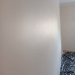BadBud - Świeżo pomalowana ściana w odcieniach beżu, widoczna listwa przypodłogowa i zabezpieczona podłoga folią malarską.