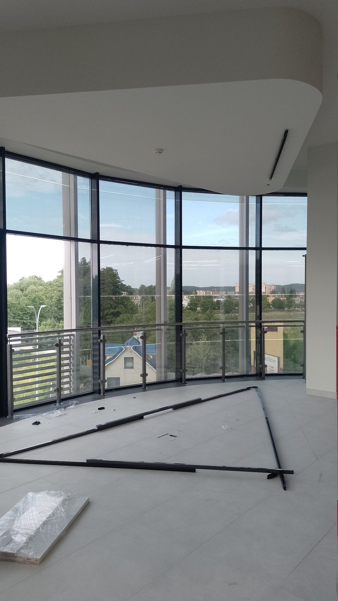 Wnętrze z panoramicznymi oknami i widokiem na zewnątrz, elementy konstrukcyjne ułożone na podłodze, przygotowania do montażu.