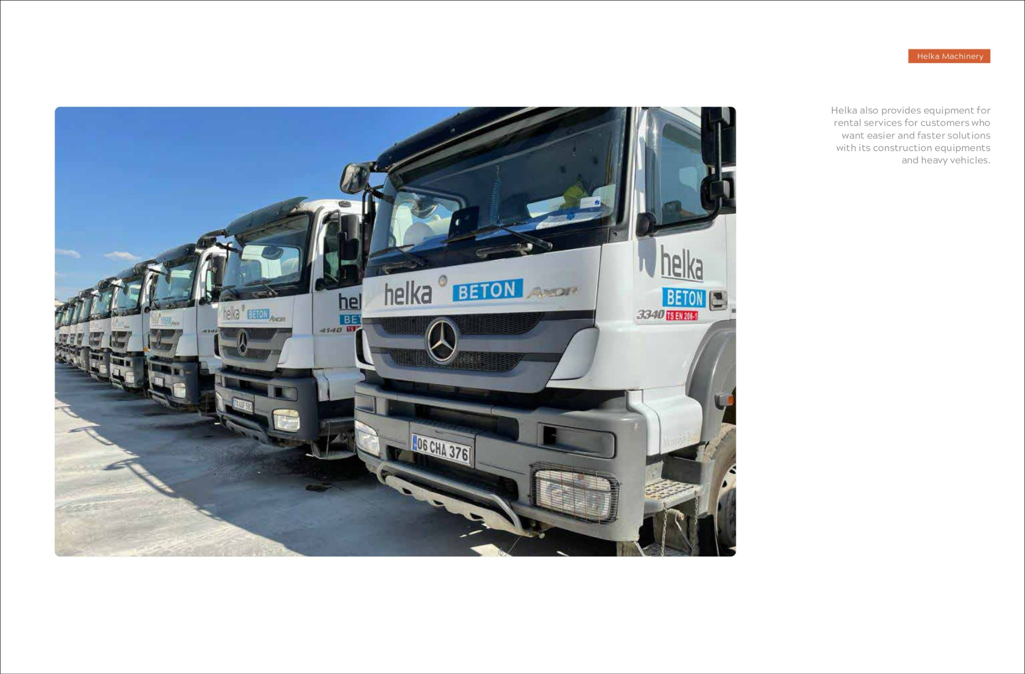 Flota białych ciężarówek z logo Helka Beton zaparkowana na placu, widok z przodu na pierwszy plan z numerami rejestracyjnymi, niebieskie niebo w tle.