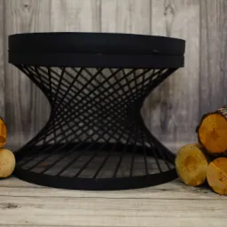 Metalowy kosz na drewno kominkowe o spiralnej konstrukcji, otoczony ułożonymi kłodami drewna na drewnianym tle.