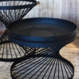 Dwie metalowe, czarne podstawki z okrągłymi blatami i spiralnymi nogami ustawione na drewnianej podłodze na tle drewnianej ściany.