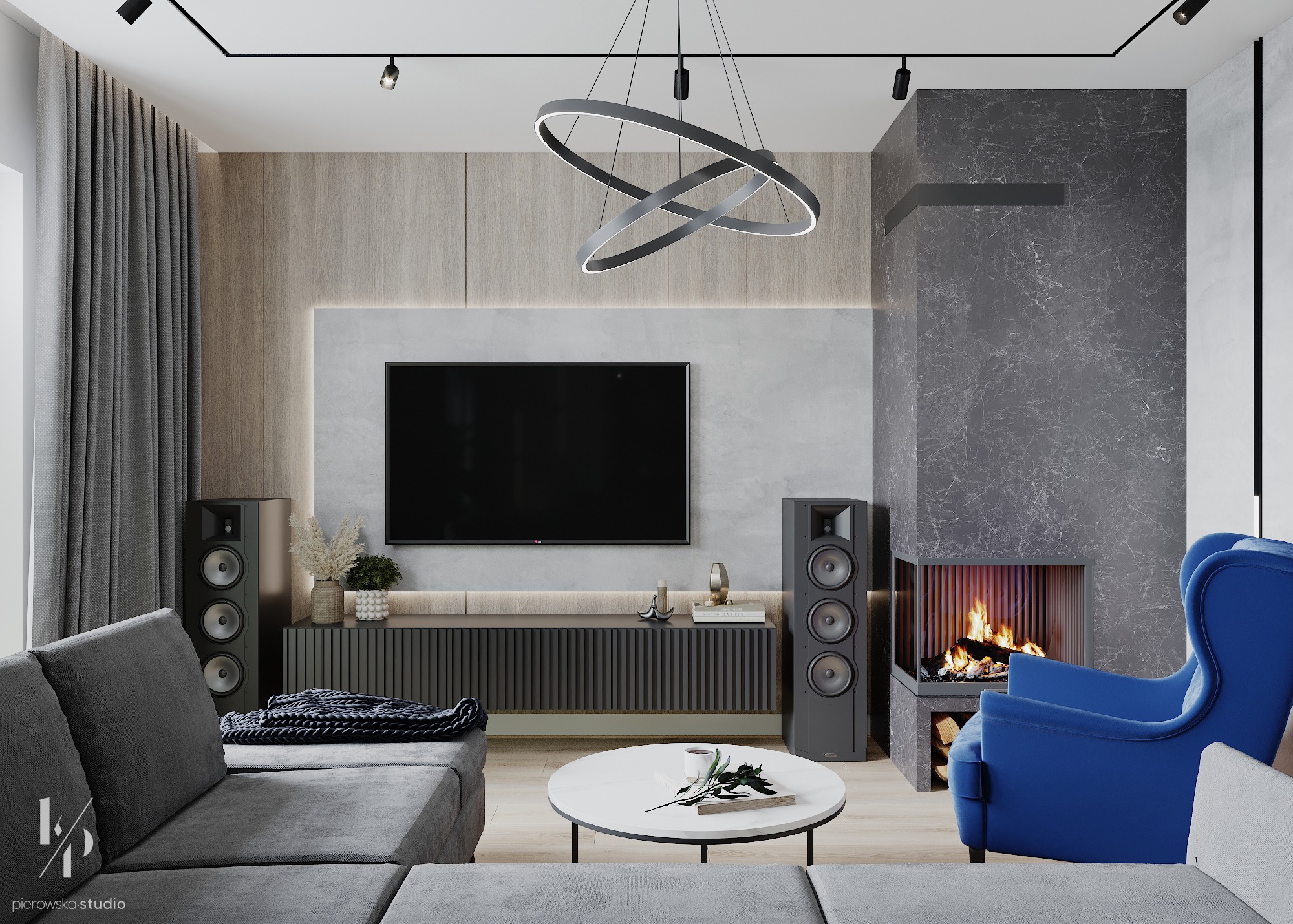 Nowoczesny salon z szarym narożnikiem, okrągłym stolikiem kawowym, telewizorem nad szafką RTV i marmurowym kominkiem narożnym oraz niebieskim fotelem uszakiem, oświetlony wiszącą lampą pierścieniową.