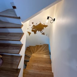 Comfort Lux - Drewniane schody spiralne z oświetleniem punktowym i dekoracją ścienną w postaci mapy świata z drewna.