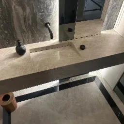 Nowoczesna łazienka z marmurową umywalką wpuszczoną w blat, czarną armaturą i dodatkami oraz podłogą wykończoną płytkami z czarnymi akcentami.