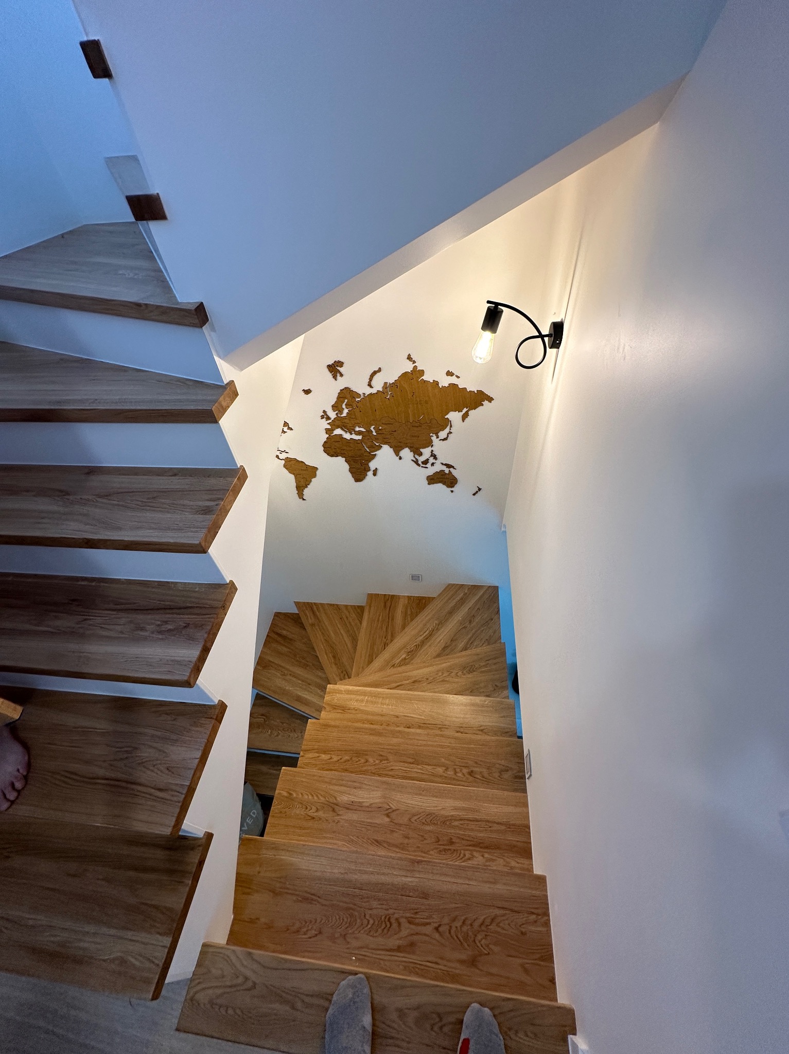 Drewniane schody spiralne z oświetleniem punktowym i dekoracją ścienną w postaci mapy świata z drewna.