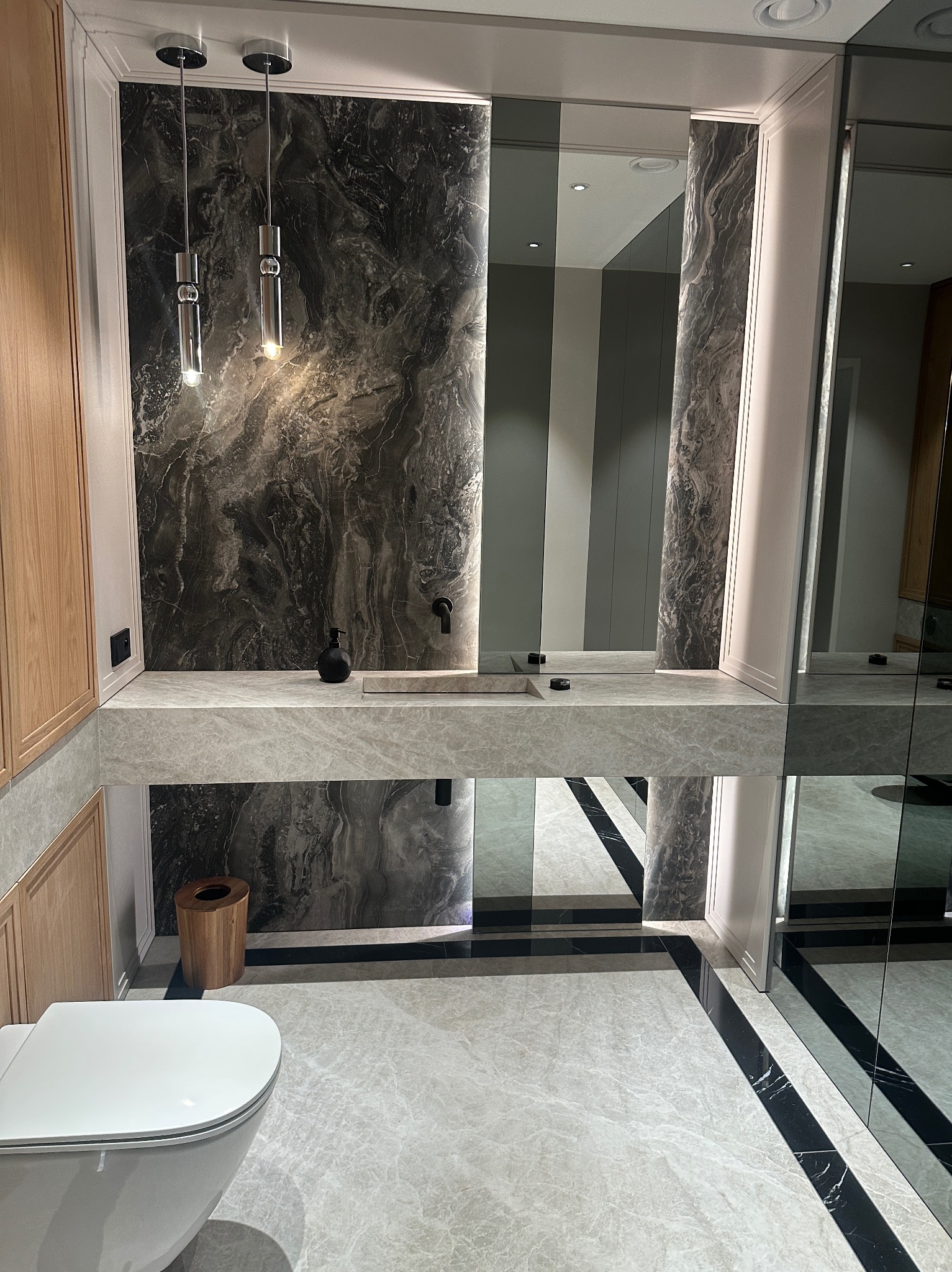 Nowoczesna łazienka w Warszawie z marmurową ścianą, blatem i podłogą, minimalistyczną armaturą i wiszącymi lampami, odbijająca się w dużym lustrze.