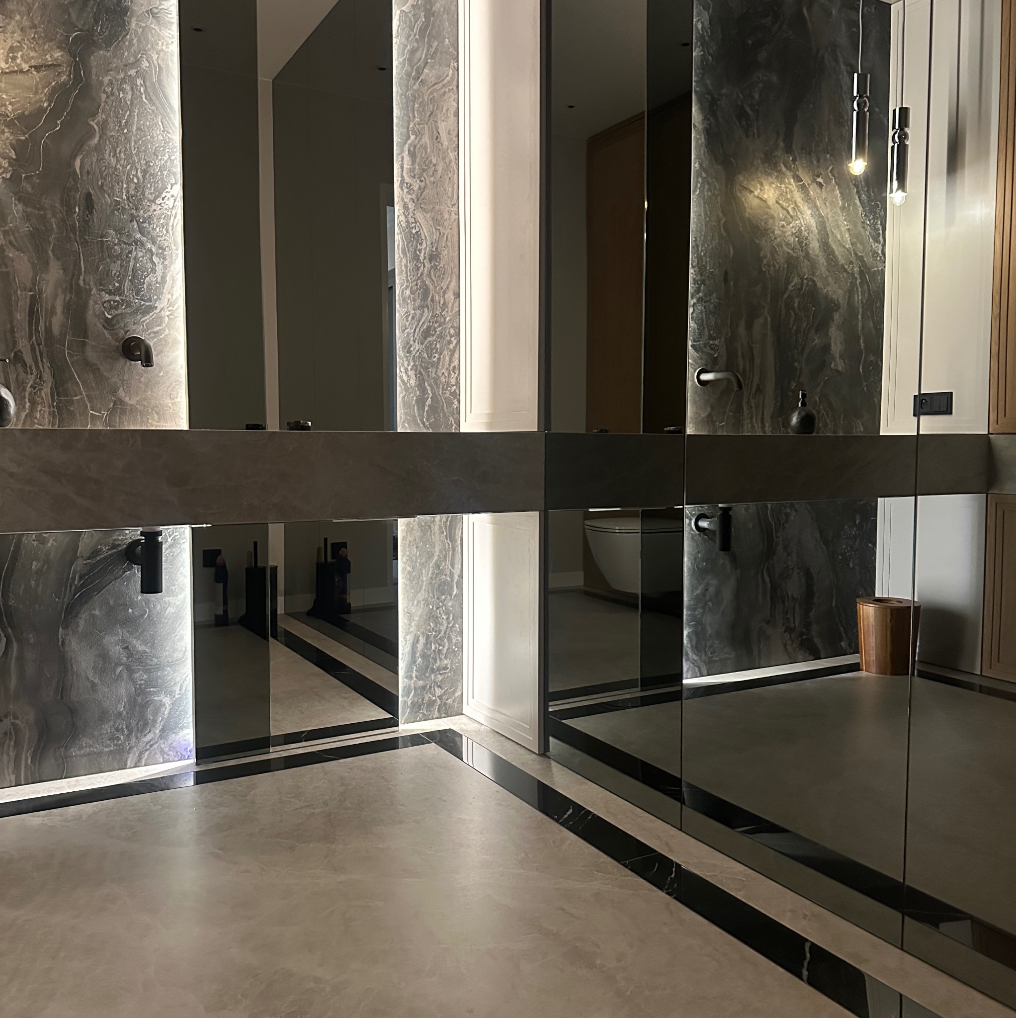 Nowoczesna łazienka z marmurowymi ścianami, podświetlanymi panelami i elementami z lustrami, z widoczną toaletą i drewnianym koszem.