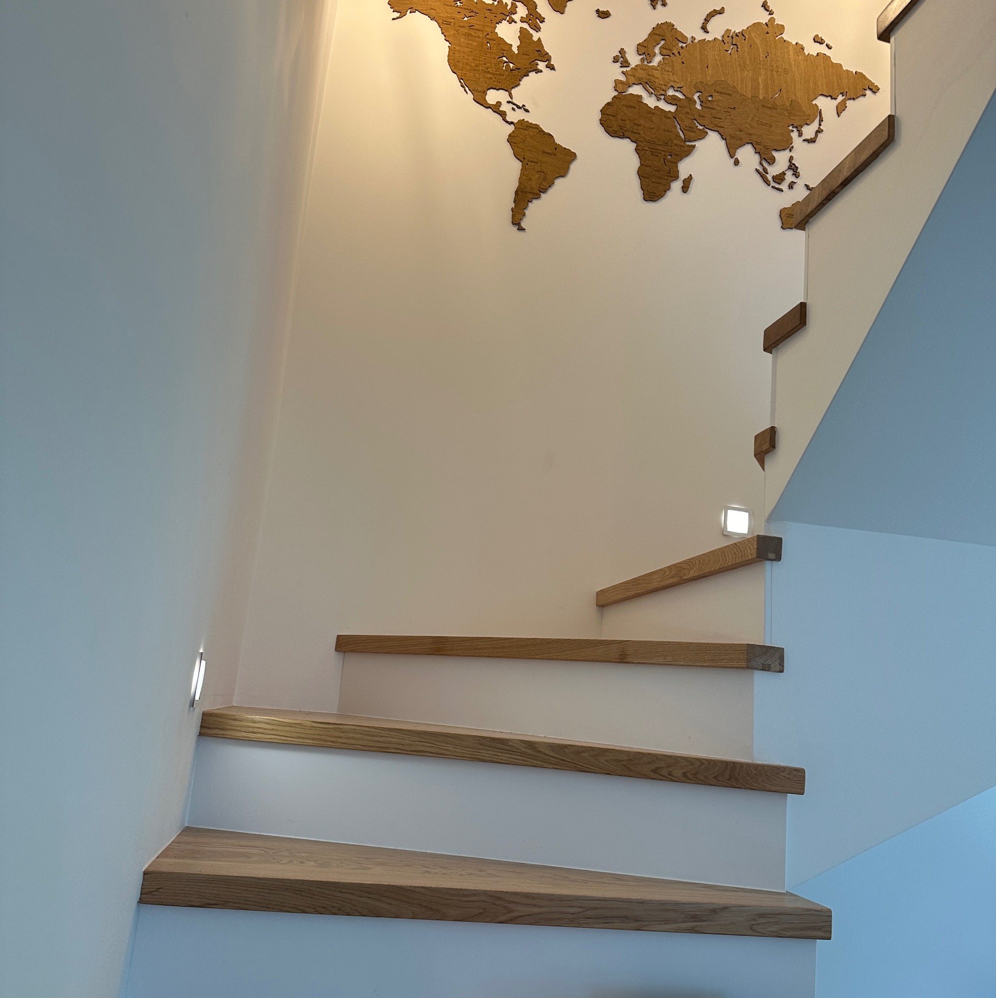 Nowoczesne schody drewniane z podświetleniem LED w ścianie, na ścianie dekoracja w postaci drewnianej mapy świata