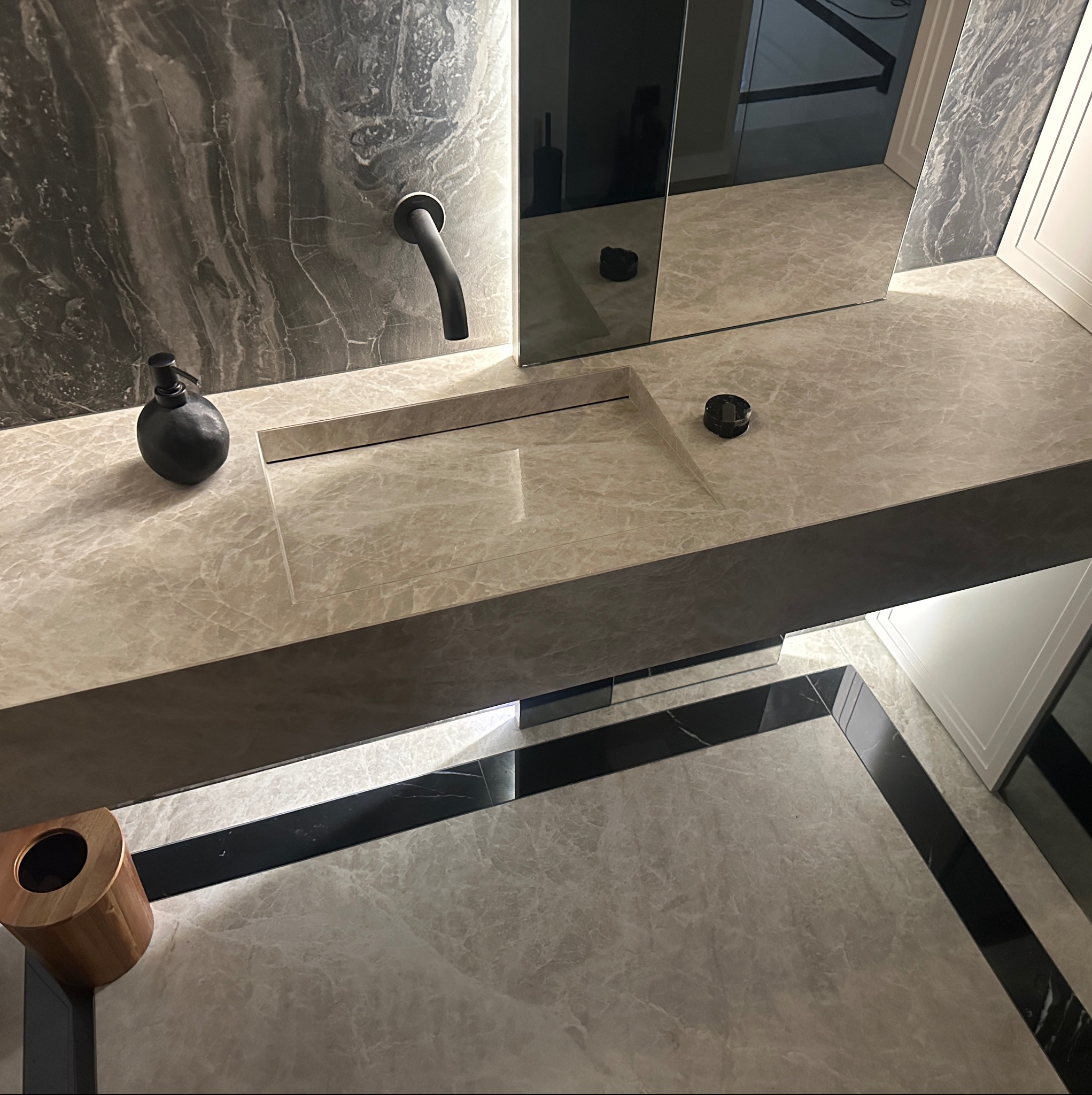 Nowoczesna łazienka z marmurową umywalką wpuszczoną w blat, czarną armaturą i dodatkami oraz podłogą wykończoną płytkami z czarnymi akcentami.