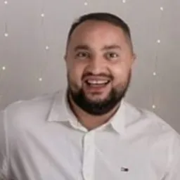 Uśmiechnięty mężczyzna w białej koszuli na tle światełek, trzymający w dłoniach schemat instalacji elektrycznej.