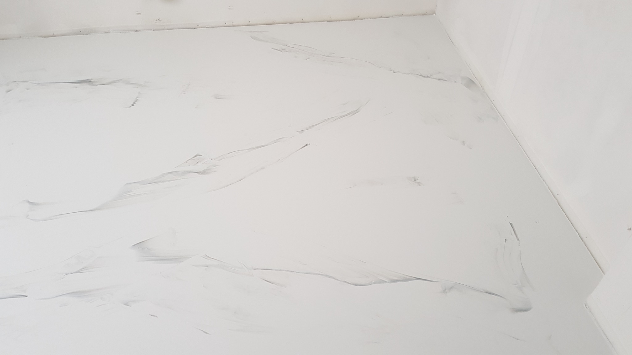 Biała, błyszcząca podłoga z szarymi, marmurkowymi wzorami w rogu pomieszczenia.