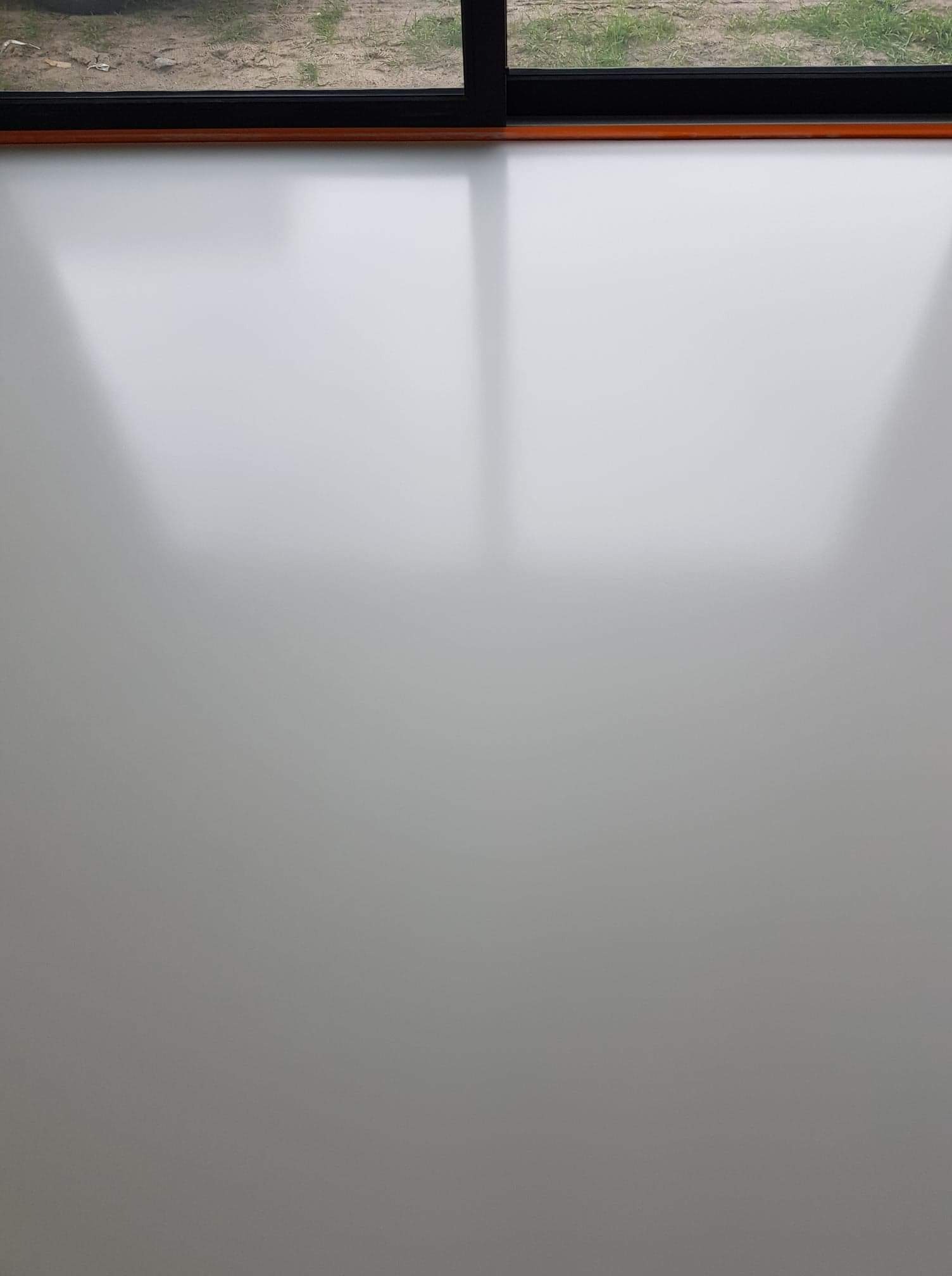 Biała, gładka powierzchnia podłogi z widocznym odbiciem światła, u góry fragment okna z widokiem na zewnątrz.