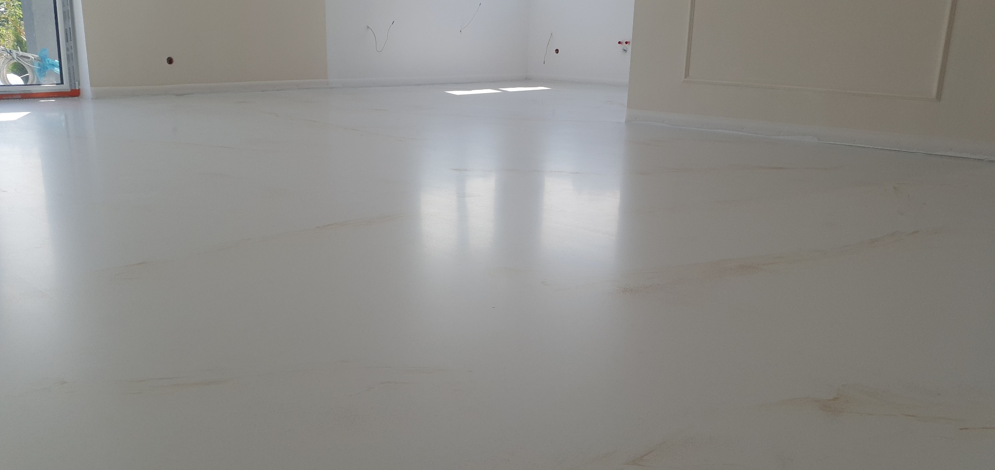 Jasna, błyszcząca podłoga z subtelnymi, marmurkowymi wzorami w odcieniach beżu, odbijająca światło w przestronnym, nowo wykończonym wnętrzu.