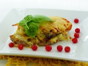 Zapiekanka z serem, ozdobiona listkiem bazylii i żurawiną, podana na białym kwadratowym talerzu z ażurową serwetką w tle.