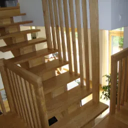 Drewniane schody z ażurową balustradą i widokiem na okno, nowoczesne wnętrze domu z naturalnym oświetleniem.