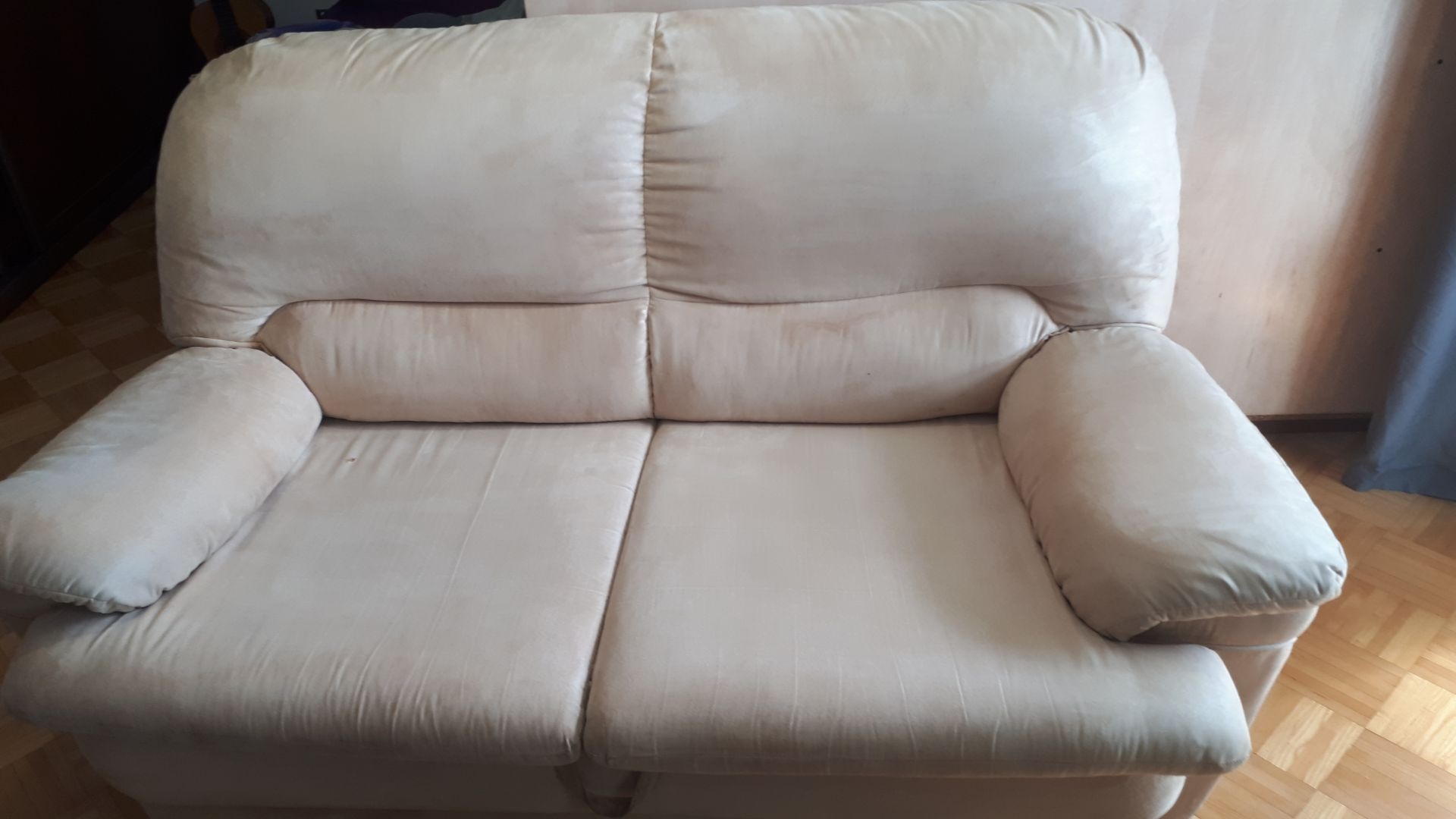 Beżowa sofa dwuosobowa z zaokrąglonymi podłokietnikami, widoczna na parkiecie w mieszkaniu w Warszawie.