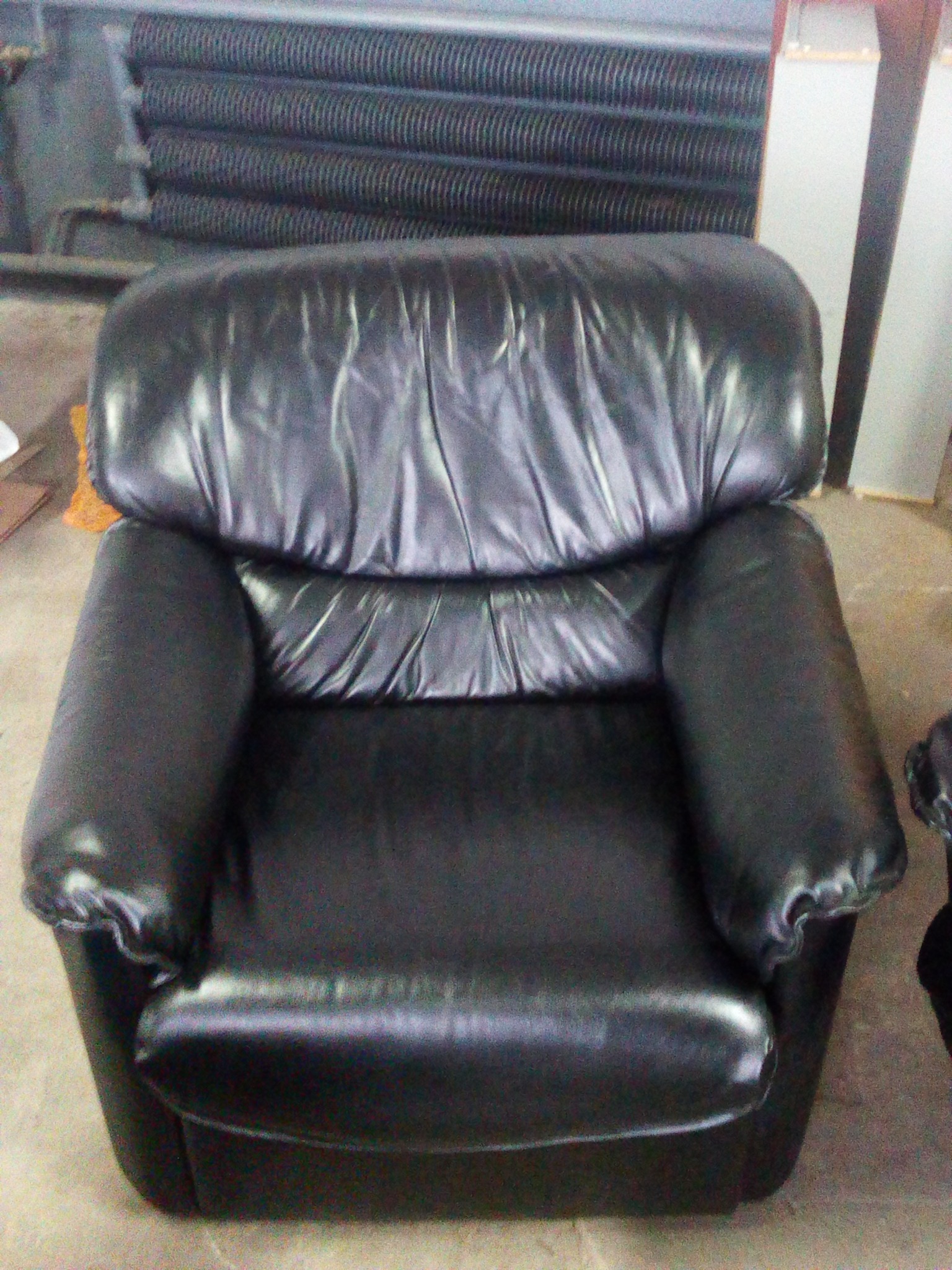 Pojedynczy fotel obity czarną skórą, widoczny z przodu, z elementami instalacji grzewczej w tle.